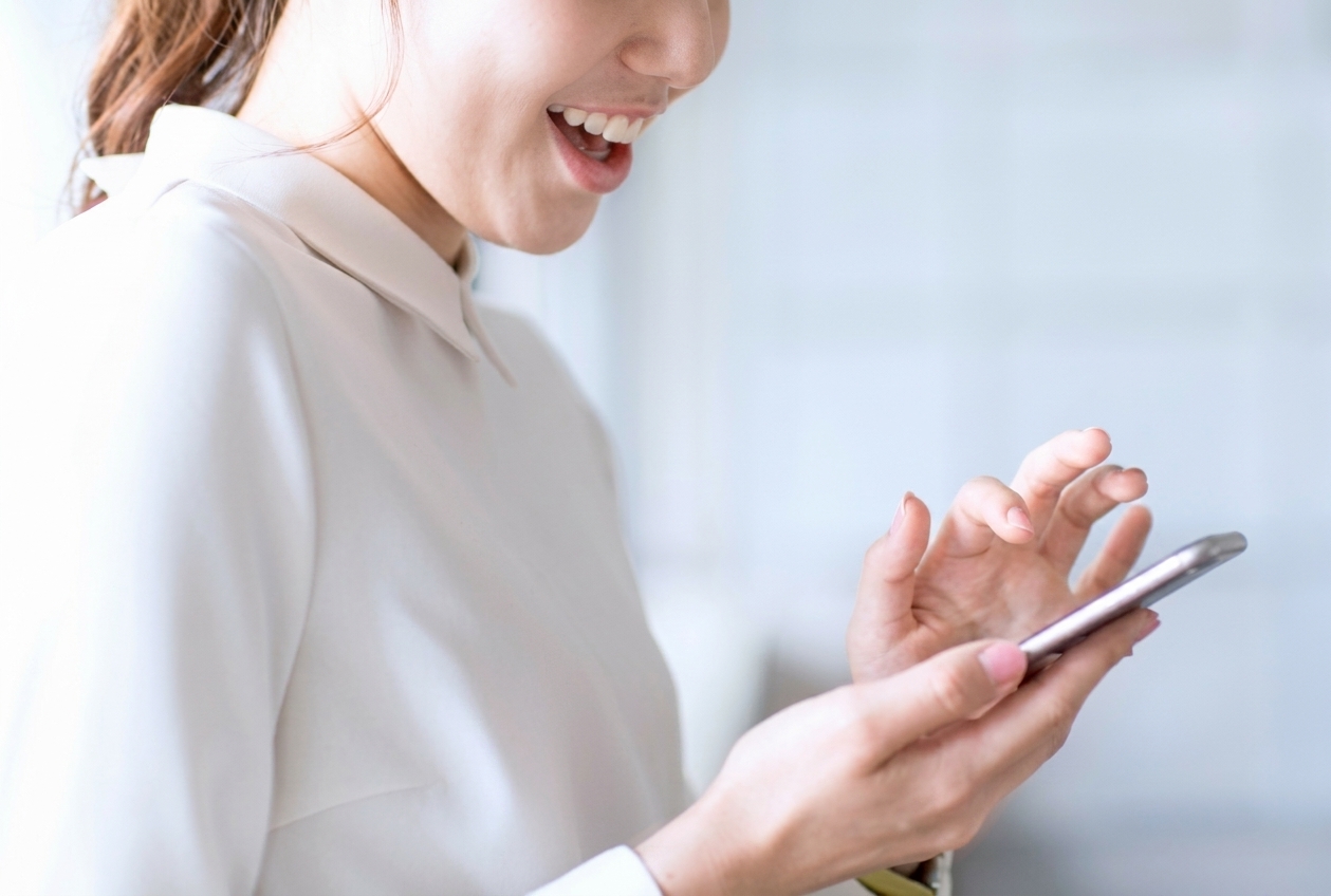 スマートフォンを操作して笑顔でクリーニングを申し込む女性